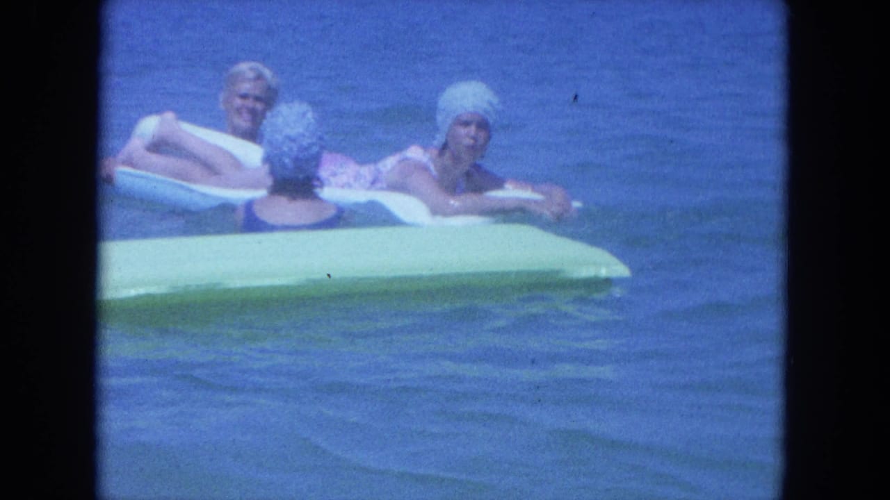 Three adult women in 1960s swimwear and caps relax on inflatable rafts in Clearwater ocean water.