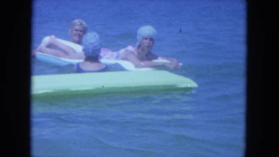 Three adult women in 1960s swimwear and caps relax on inflatable rafts in Clearwater ocean water.