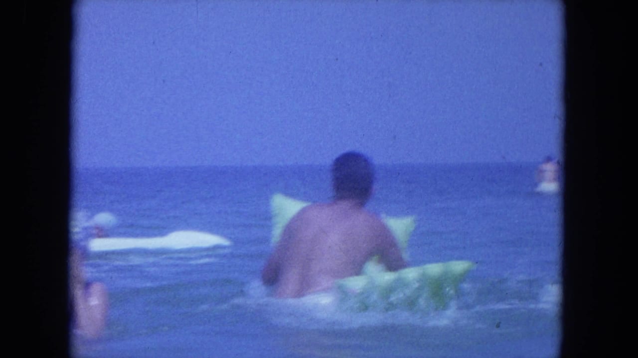 Man faces away while floating or pushing a green inflatable raft in calm ocean water.