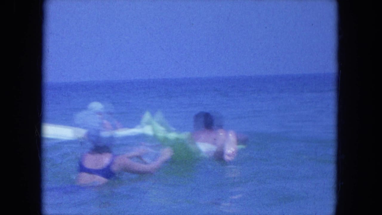 Clearwater beach footage from 1964 shows adults in the surf around a green inflatable float, with another swimmer on a white float in the background.