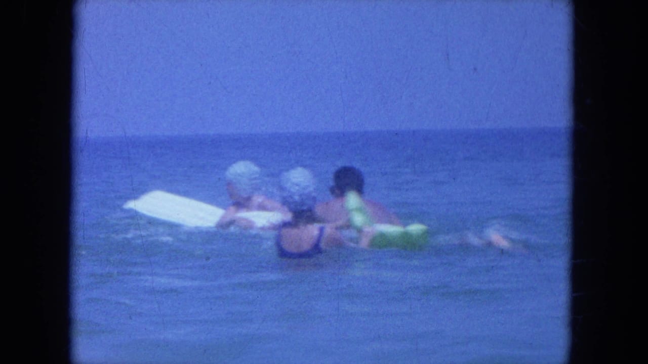 1964 Clearwater, Florida home-movie frame with three swimmers near a white board in calm open water.