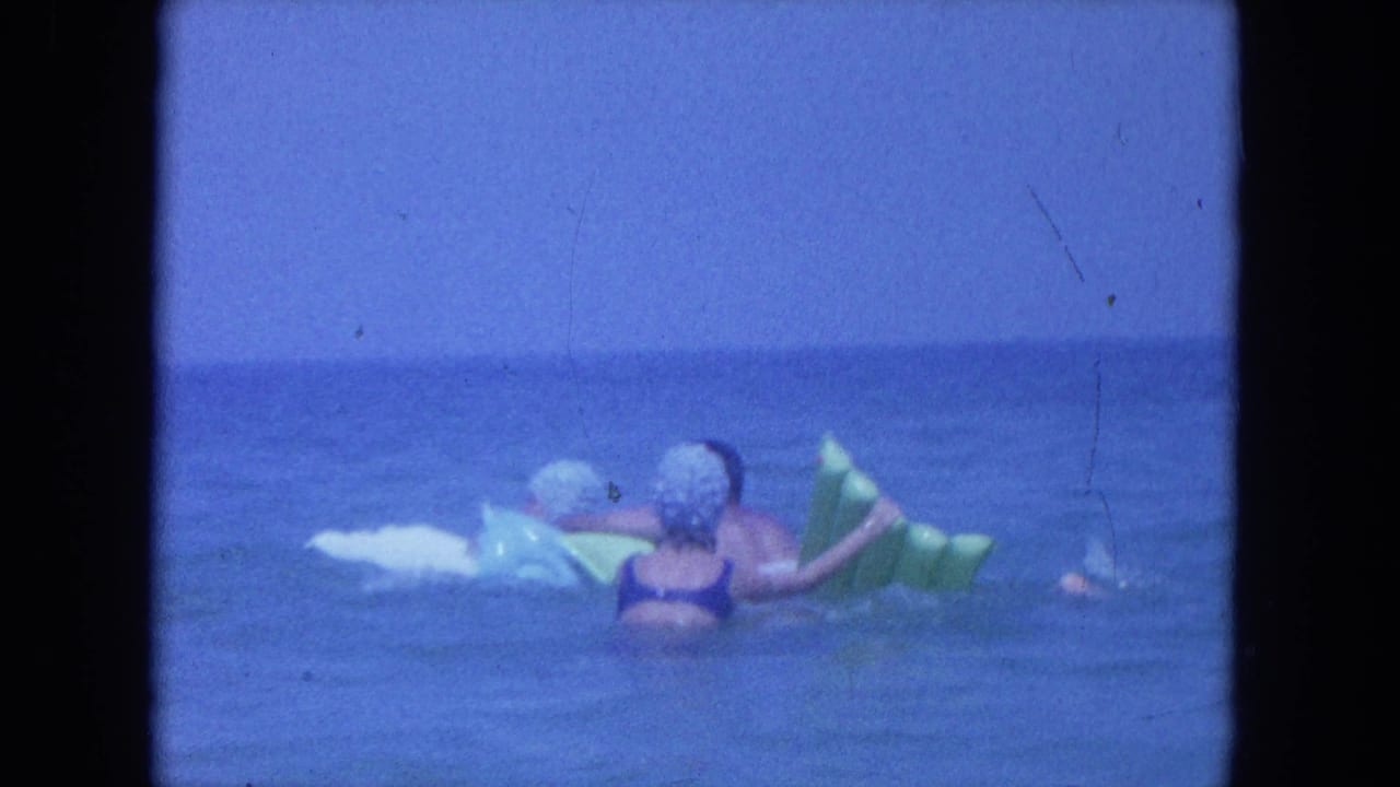 1964 Clearwater, Florida frame showing a woman in a swim cap near a green inflatable float and white board in open water.