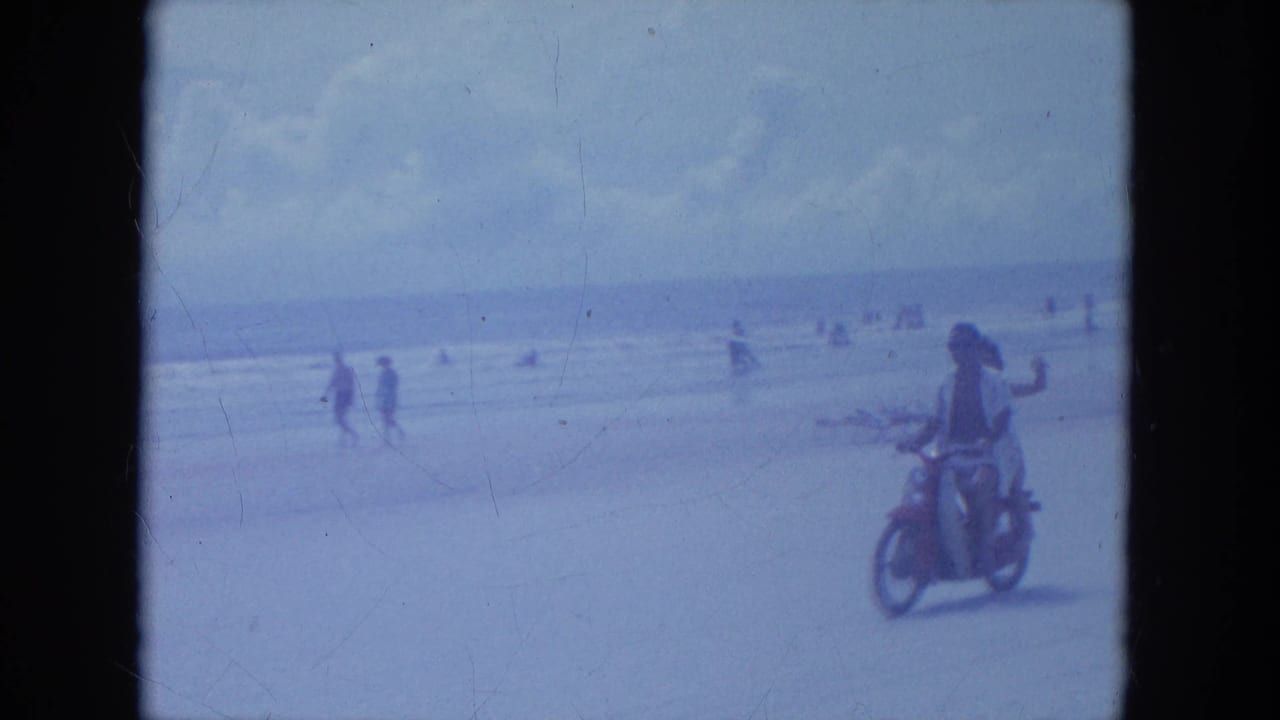 Two riders pass closer to camera on the Clearwater beach, and the passenger raises a hand in a casual wave.