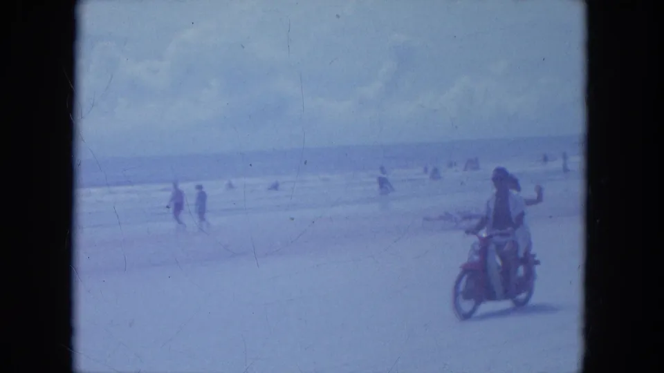Two riders pass closer to camera on the Clearwater beach, and the passenger raises a hand in a casual wave.