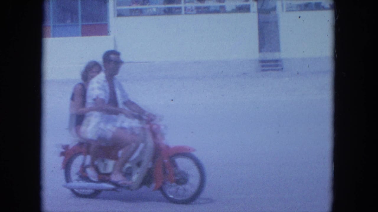 The couple continues past the camera on a red motorcycle in the supplied 1964 Clearwater beachside home-movie footage.