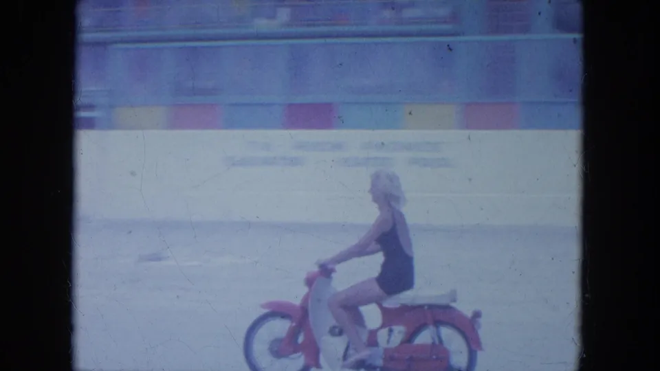 The rider continues along the Clearwater beach sand on a small red-and-white motorbike, filmed in soft faded 8mm color.