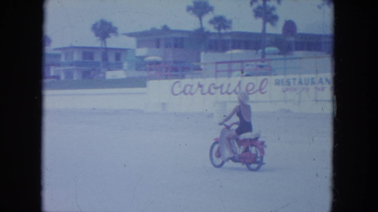 Near the end of the clip, the rider is smaller in frame as she passes a wall with Carousel restaurant wording and beach buildings behind it.