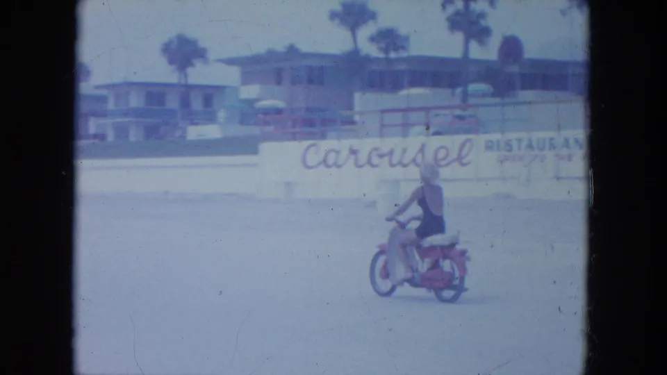 Near the end of the clip, the rider is smaller in frame as she passes a wall with Carousel restaurant wording and beach buildings behind it.