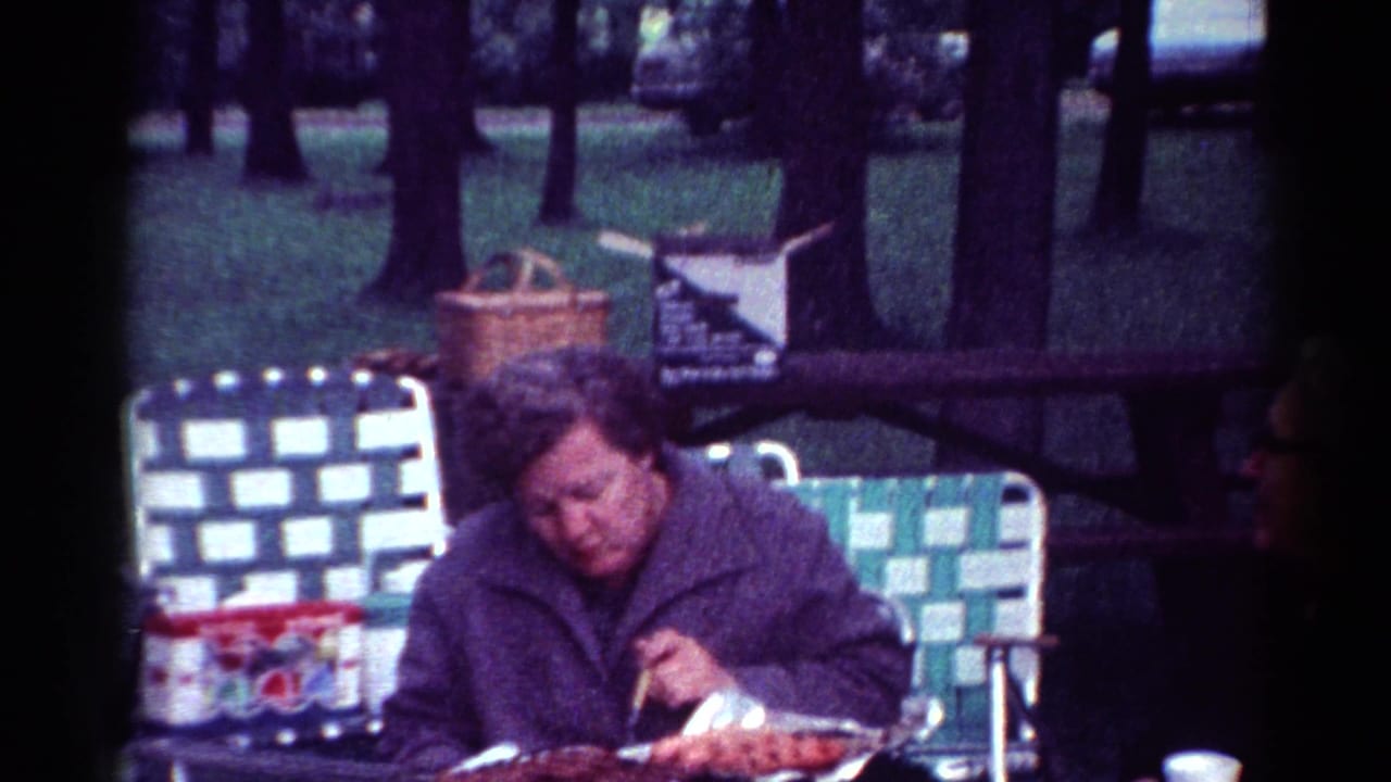 Woman eating at a picnic table in a wooded park while a man sits beside her.