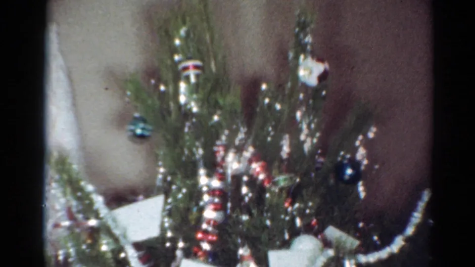 Small tinsel Christmas tree with shiny ornaments and nearby packages in a 1964 Cleveland home-movie interior.