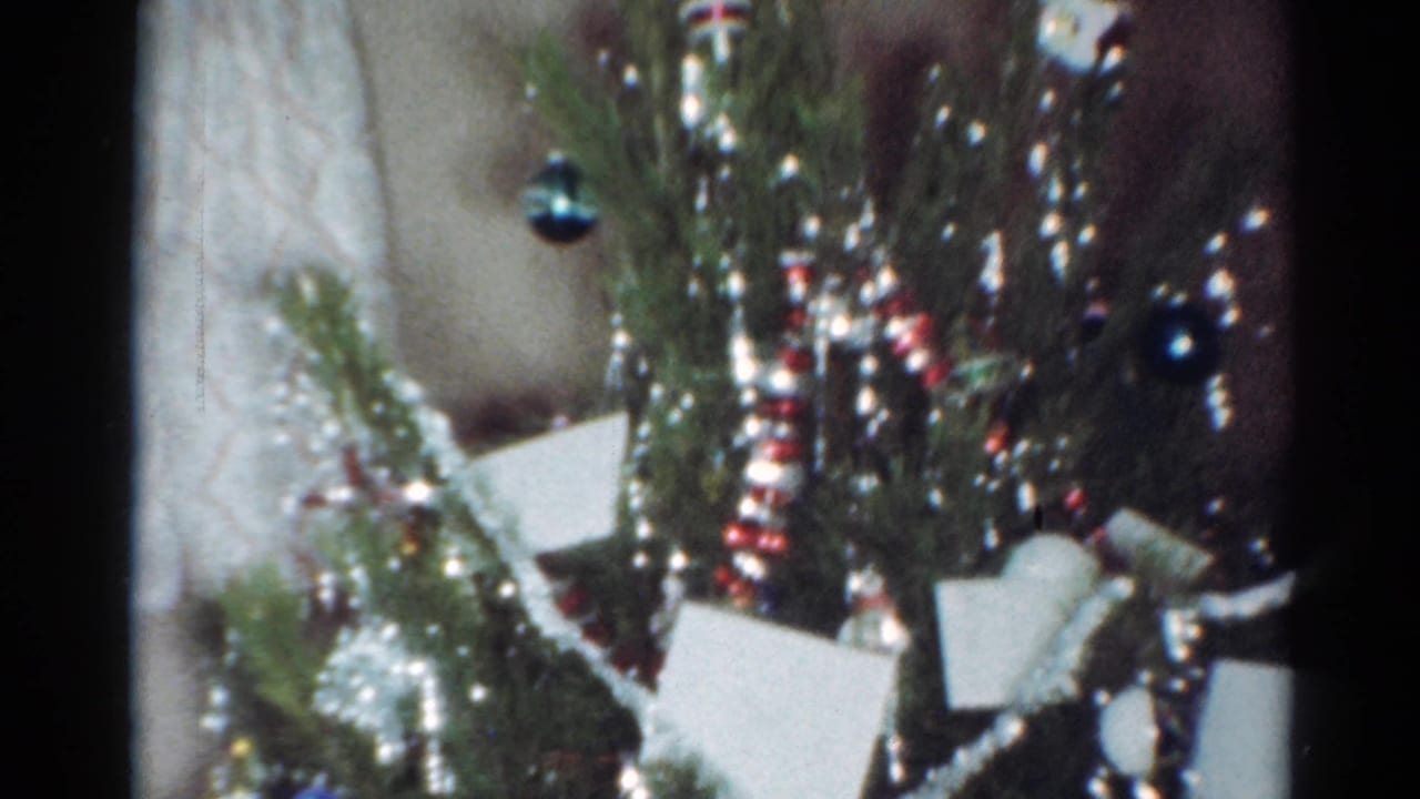 1964 Cleveland home-movie frame showing a close Christmas tree detail with silver tinsel, colored ornaments, striped garland, and small white cards.