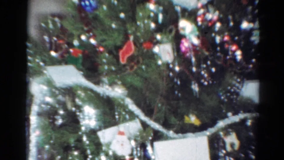 1964 Cleveland 8mm frame showing a dense close-up of a Christmas tree with silver tinsel, colored ornaments, and several white card-like pieces.
