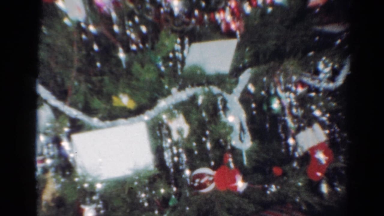 1964 Cleveland home-movie frame showing a close-up Christmas tree with tinsel, red ornaments, white ribbon, and gifts below.