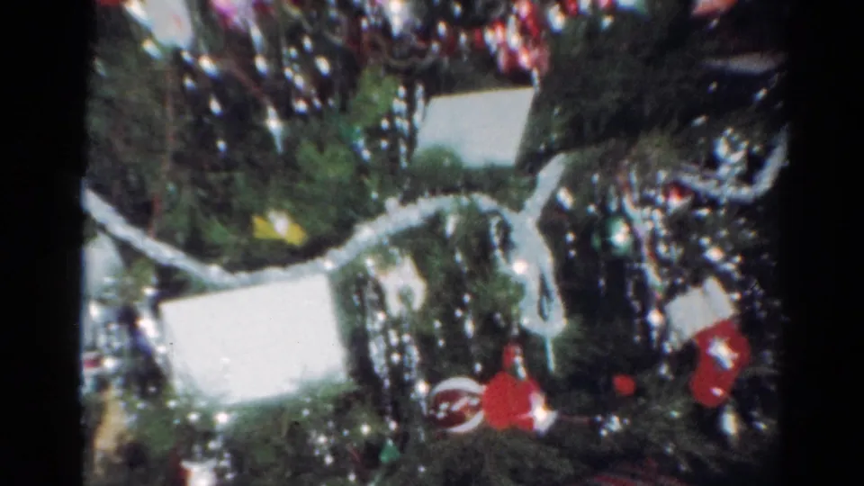1964 Cleveland home-movie frame showing a close-up Christmas tree with tinsel, red ornaments, white ribbon, and gifts below.