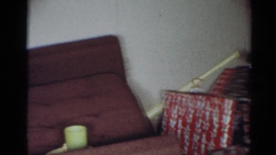 1964 Cleveland home interior showing a brown upholstered chair, stacked wrapped gifts, a pale cup or container, and a plain wall.