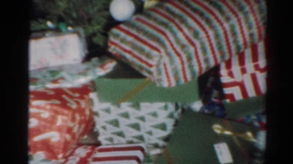 1964 Cleveland home-movie frame showing wrapped presents near holiday greenery and a small card or tag.