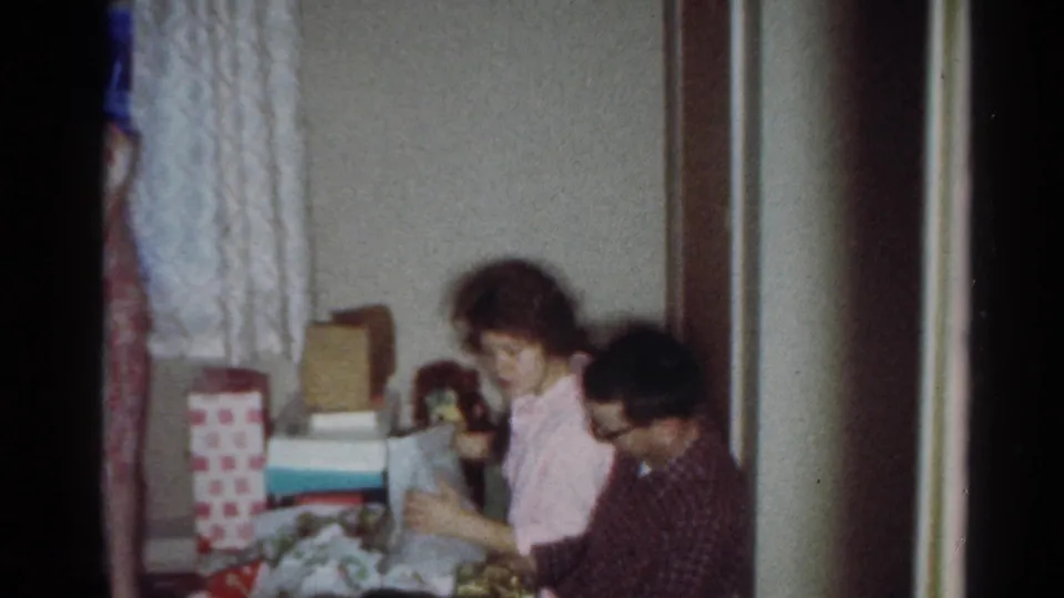 1964 Cleveland home interior showing seated family members handling gifts near patterned curtains and stacked boxes.