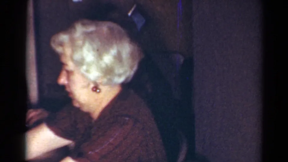 Older woman with styled white hair and earrings sits in profile in a dim Cleveland home interior, 1964.