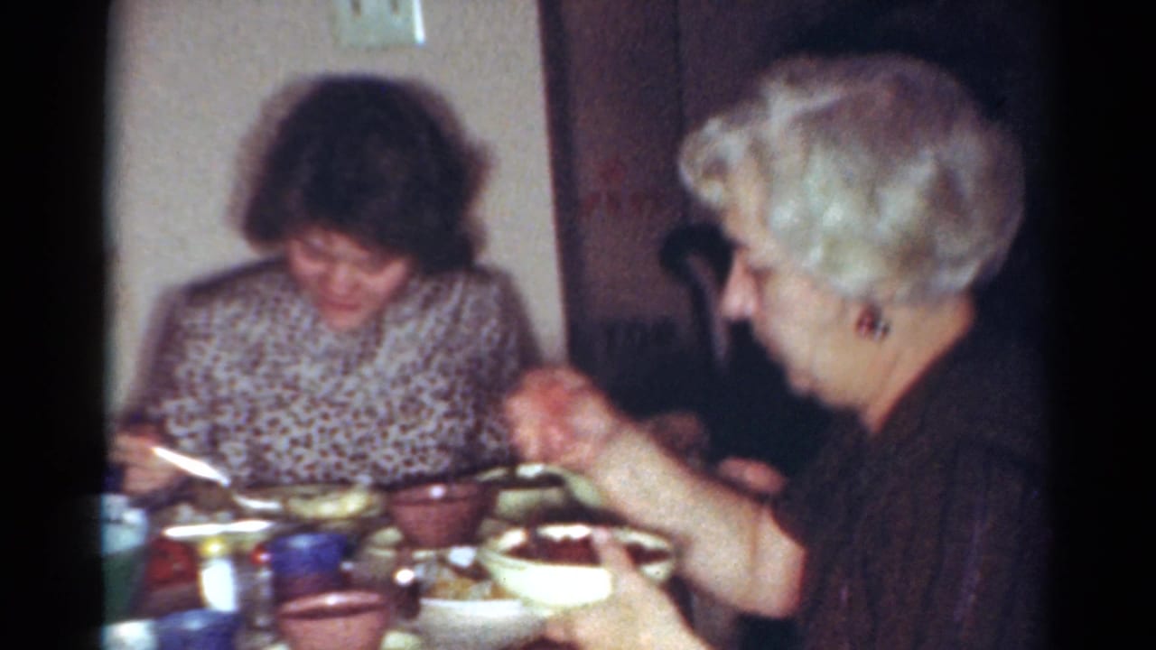 Two adult women seated at a dining table with bowls, cups, utensils, and serving dishes.