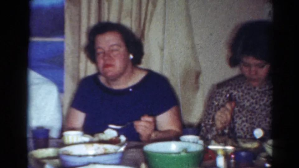 Two adult women remain seated at the Cleveland home dinner table, with tableware and curtains visible in the 8mm frame.