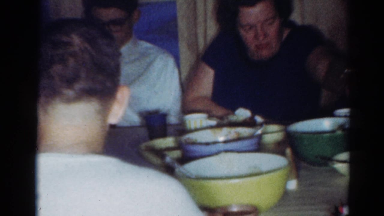 Family members seated around a dinner table with bowls, plates, and cups visible.