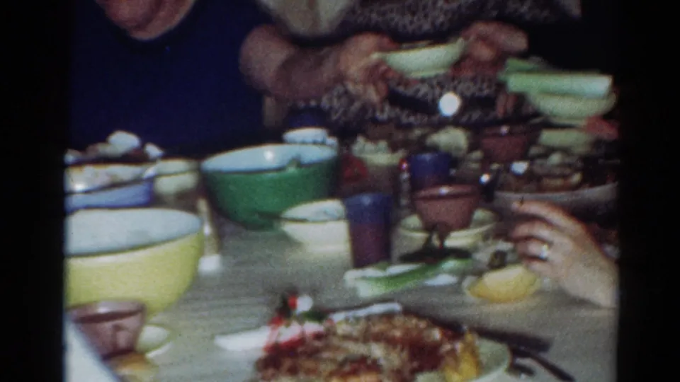 1964 Cleveland home interior with a crowded family table, visible hands, bowls, cups, and plates of food.