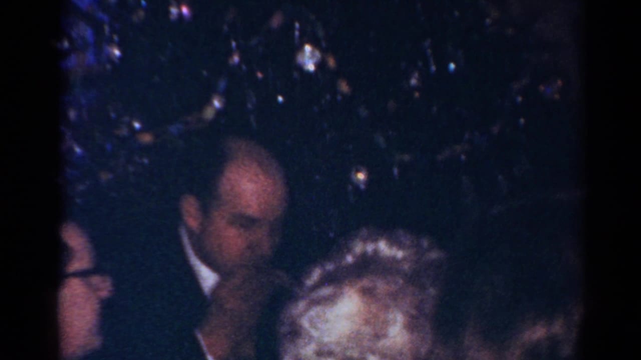 1964 Cleveland home-movie frame showing adults at a Christmas gathering beside sparkling tree decorations.