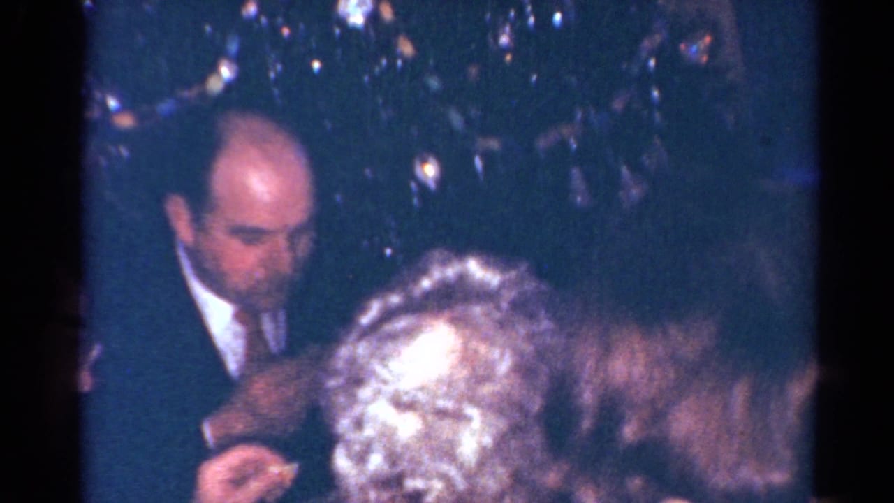 1964 Cleveland holiday dinner frame with a suited man leaning toward the table near Christmas tree lights.
