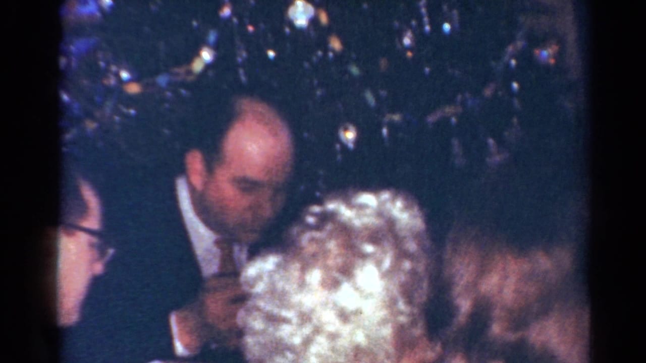 Adults in formal clothing gather indoors at a Cleveland holiday dinner, with a Christmas tree visible in the background.