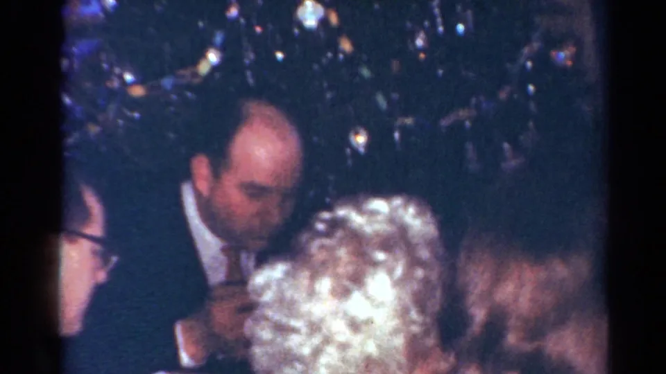 Adults in formal clothing gather indoors at a Cleveland holiday dinner, with a Christmas tree visible in the background.