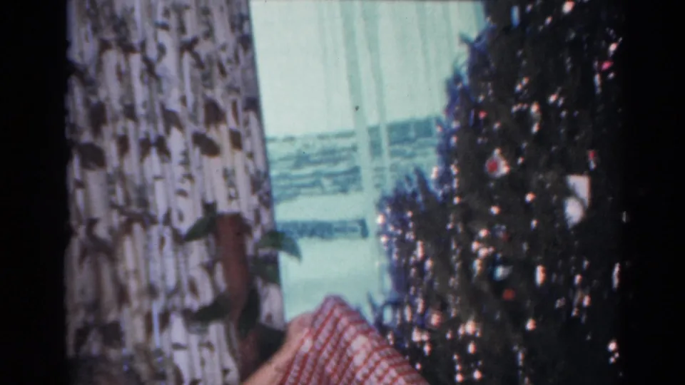 The home-movie frame shows the present moving downward near the decorated tree in the 1964 Cleveland Christmas scene.