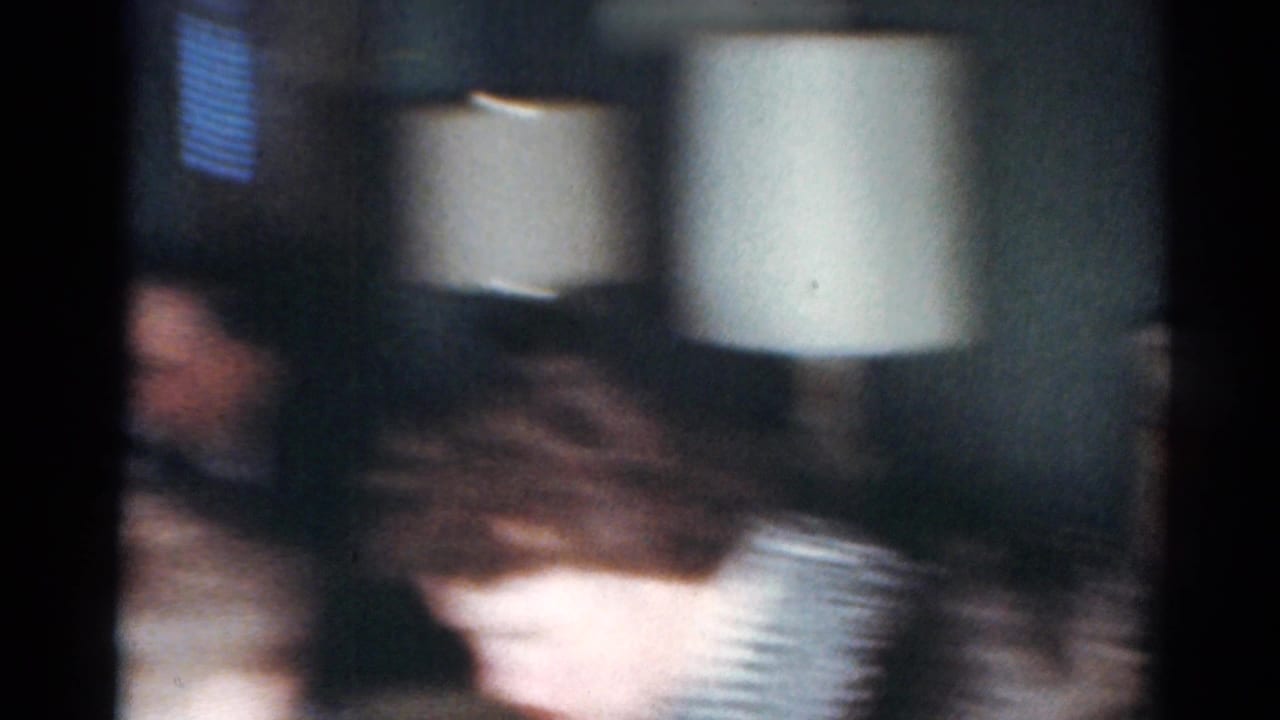 Soft-focus interior with blurred figures and a white lampshade in the background.