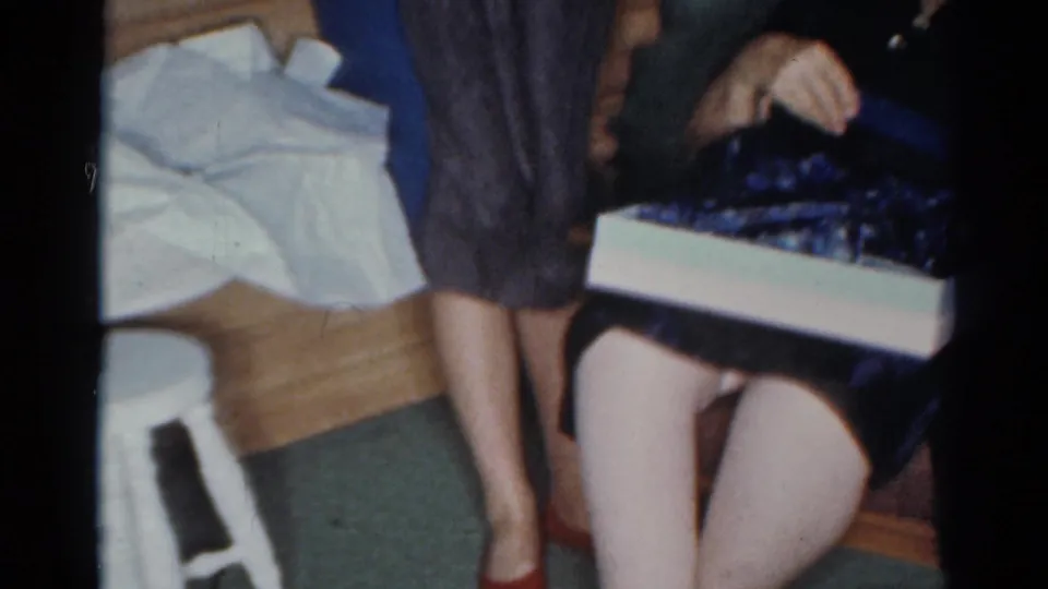 In a Cleveland 1964 home interior, an older woman sits with a box and dark garment while another woman stands nearby.