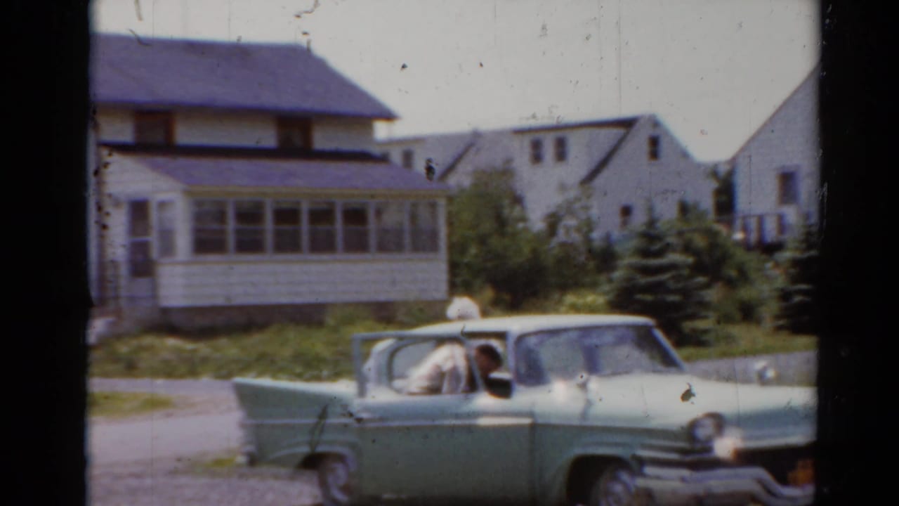 Light green sedan parked in a driveway beside white suburban houses.