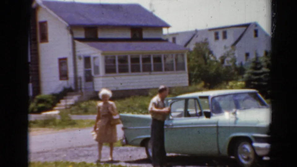 1964 Elkhart, Illinois frame showing a man and woman beside a light green sedan with the rear door open in a driveway.