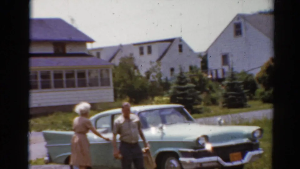 The woman appears to gesture toward the man near the parked car, with houses and shrubs behind them in Elkhart, Illinois.