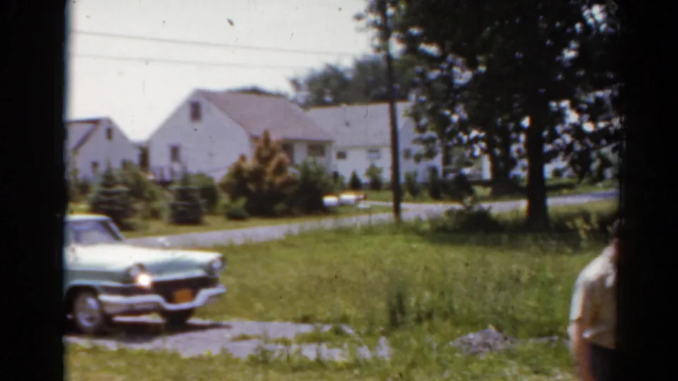 The car and residential lawn remain in view as the man exits the frame edge in this 1964 Elkhart, Illinois home-movie shot.