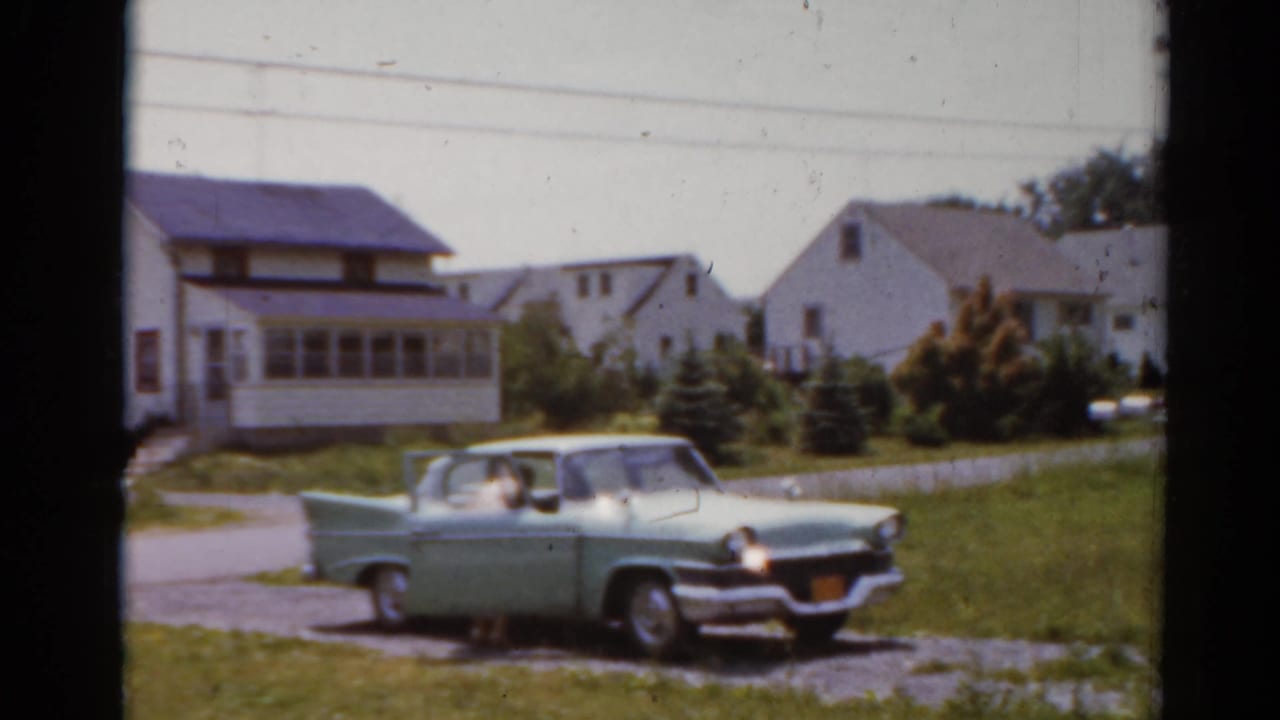 The green car is seen from farther right, parked near a lawn and residential houses in Elkhart, Illinois.