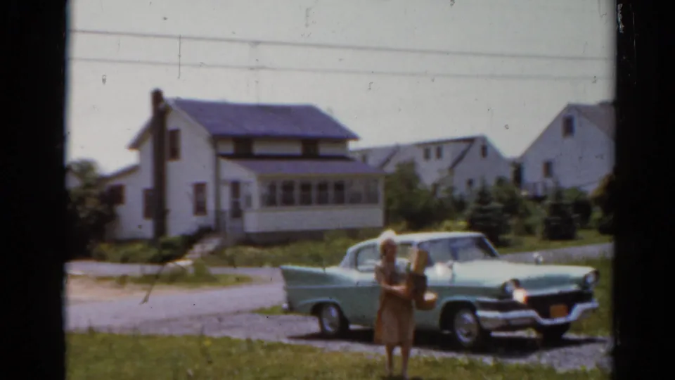 The woman and small child stand in front of the pale green car, with Elkhart houses and lawns visible behind them.