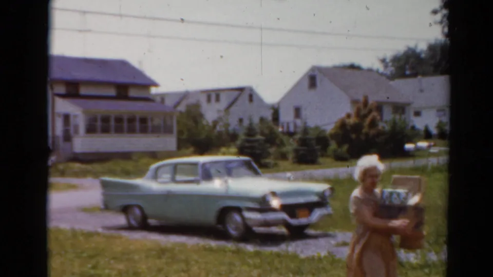 In the final frame, the woman passes close to the camera with groceries while the 1950s sedan remains parked in the driveway.