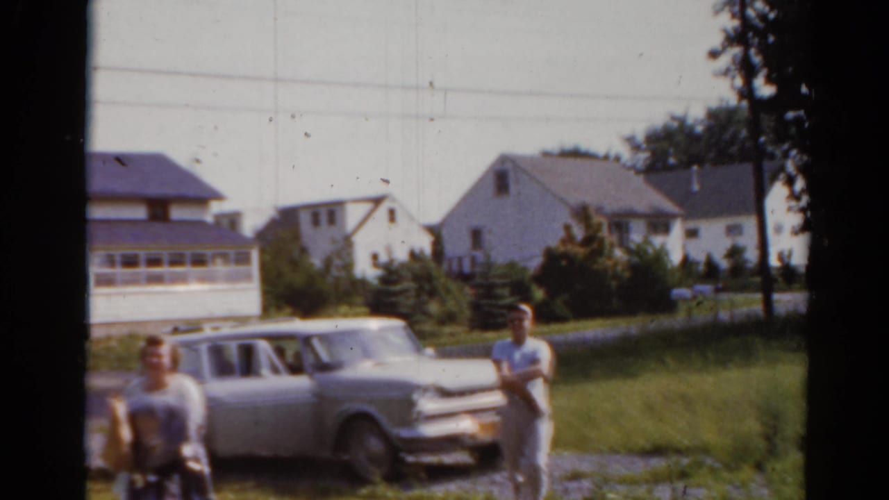 Woman with bags passes in front while a boy stands by a station wagon.