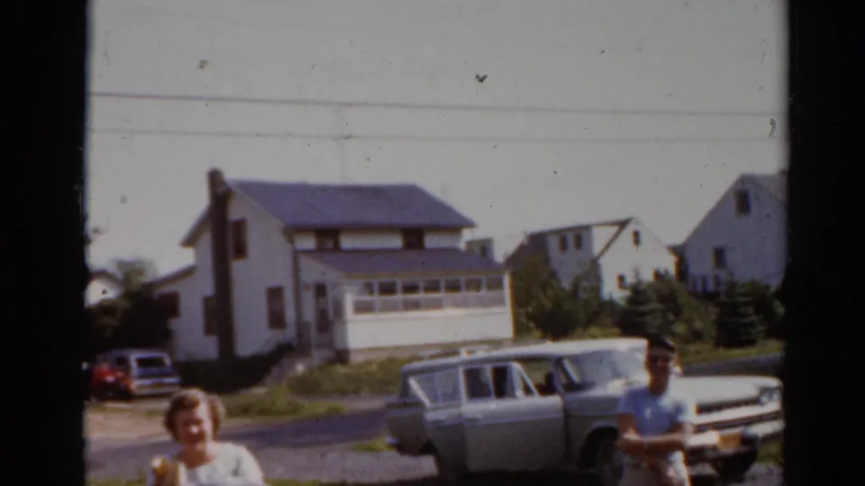 A woman carrying bags stands near the lower foreground as a boy and light station wagon remain visible against Elkhart, Illinois houses.