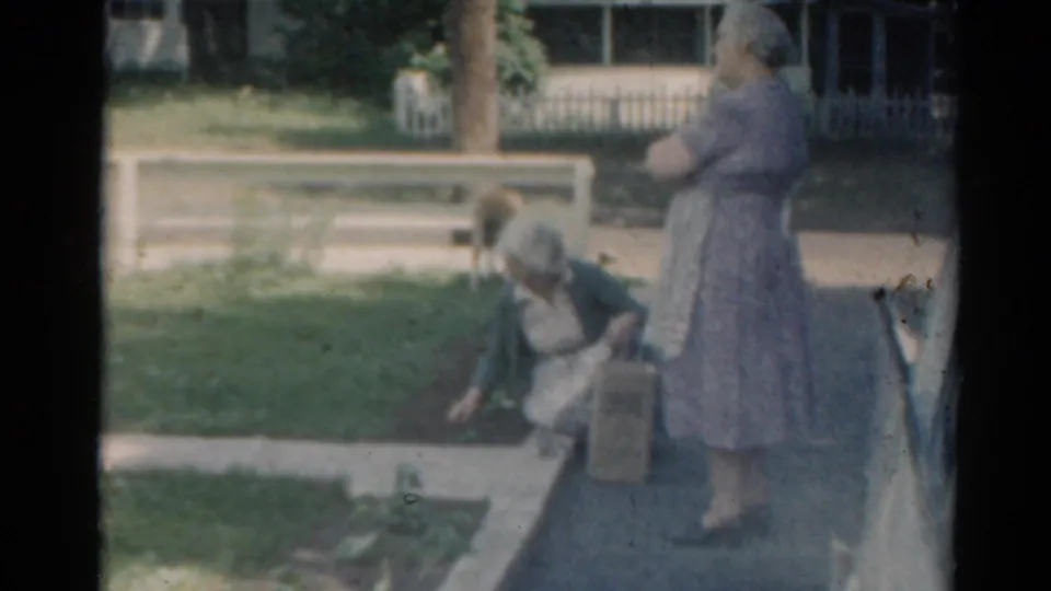 The Elkhart, Illinois yard scene continues as one woman kneels by the flowerbed and another stands near the driveway beside a mid-century car.