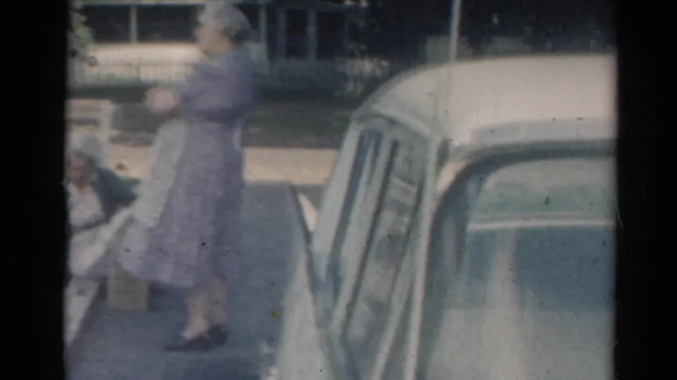 The closing frame shows the standing woman near the driveway and car, with the kneeling gardener partly cut off at the left edge.