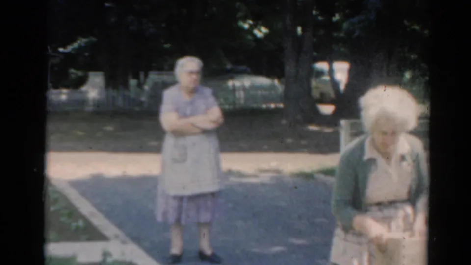 1964 Elkhart, Illinois frame showing one elderly woman in an apron and another nearer the camera carrying a paper bag.