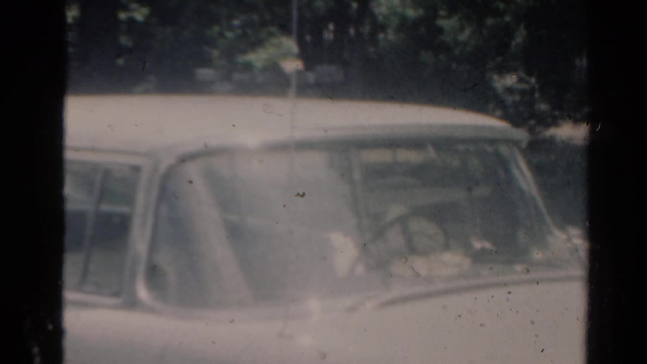Older car seen through a dusty windshield or window in soft 8mm footage.