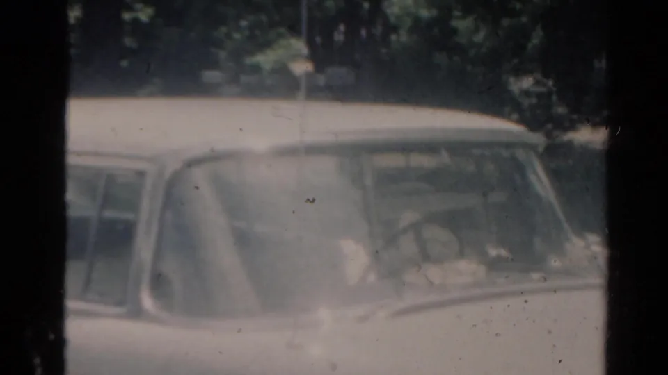 A brief 1964 Elkhart, Illinois 8mm view shows an older car partly obscured by haze, glass, and film softness.