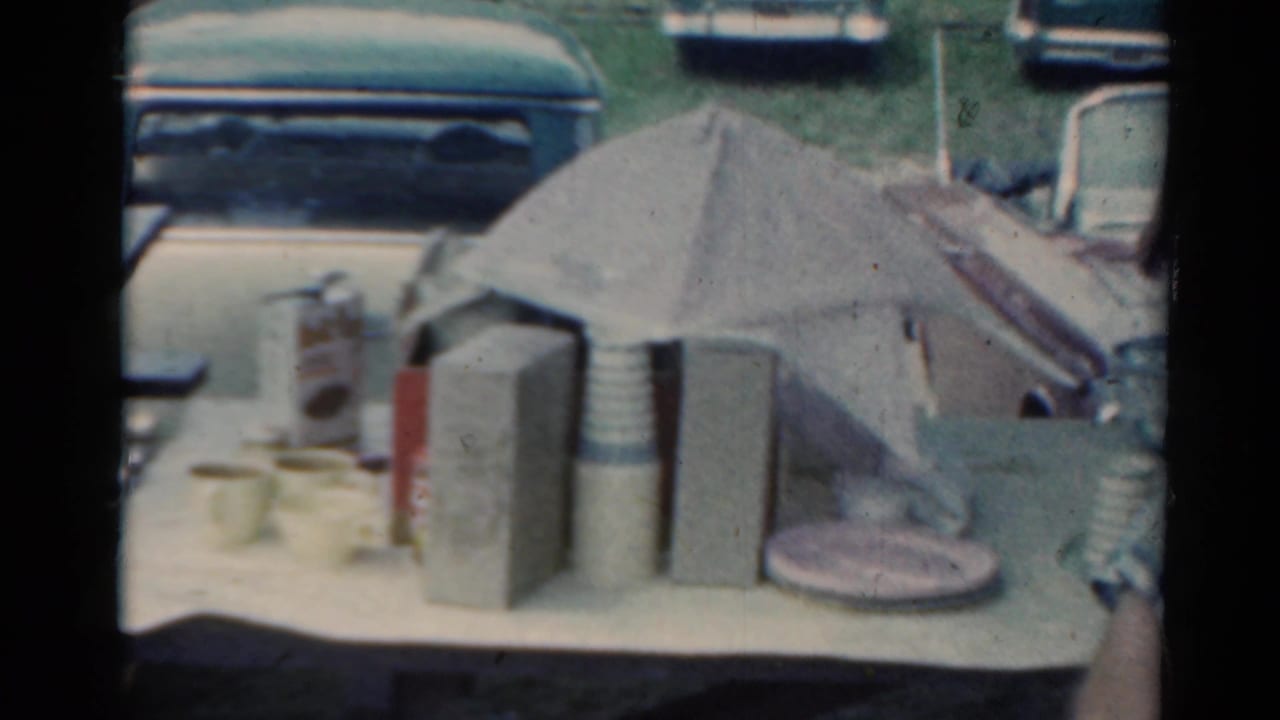 Tabletop with cups, thermos, paper umbrella, and parked cars in the background.