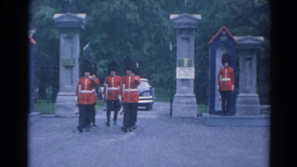 Red-coated uniformed men with rifles gather at a stone entrance in the 1964 8mm home-movie footage.