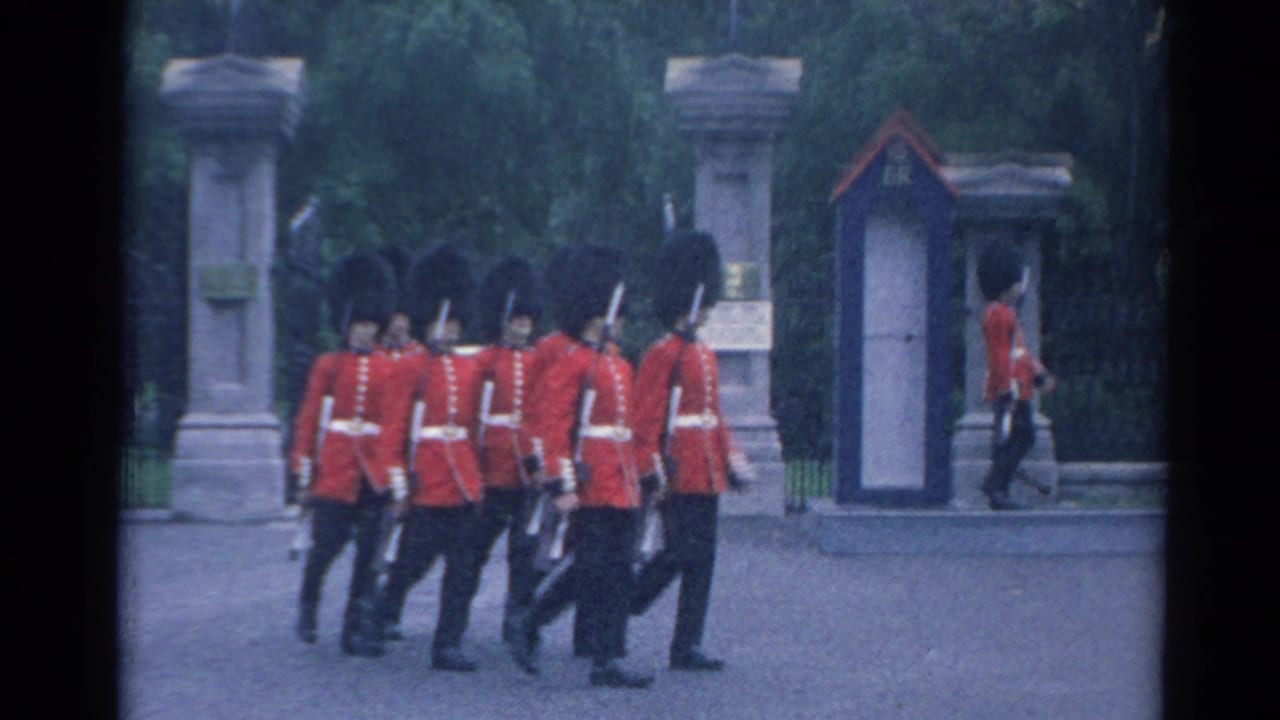 British-style guards in red tunics march near stone gateposts and trees.